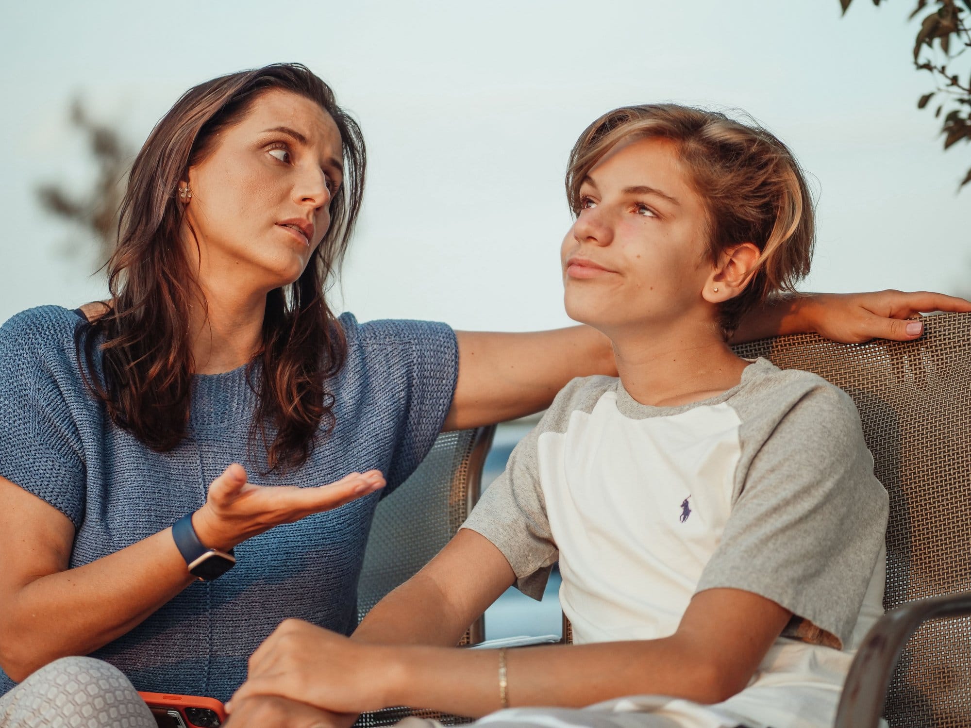 O mamă și fiul ei adolescent stau de vorbă pe o terasă