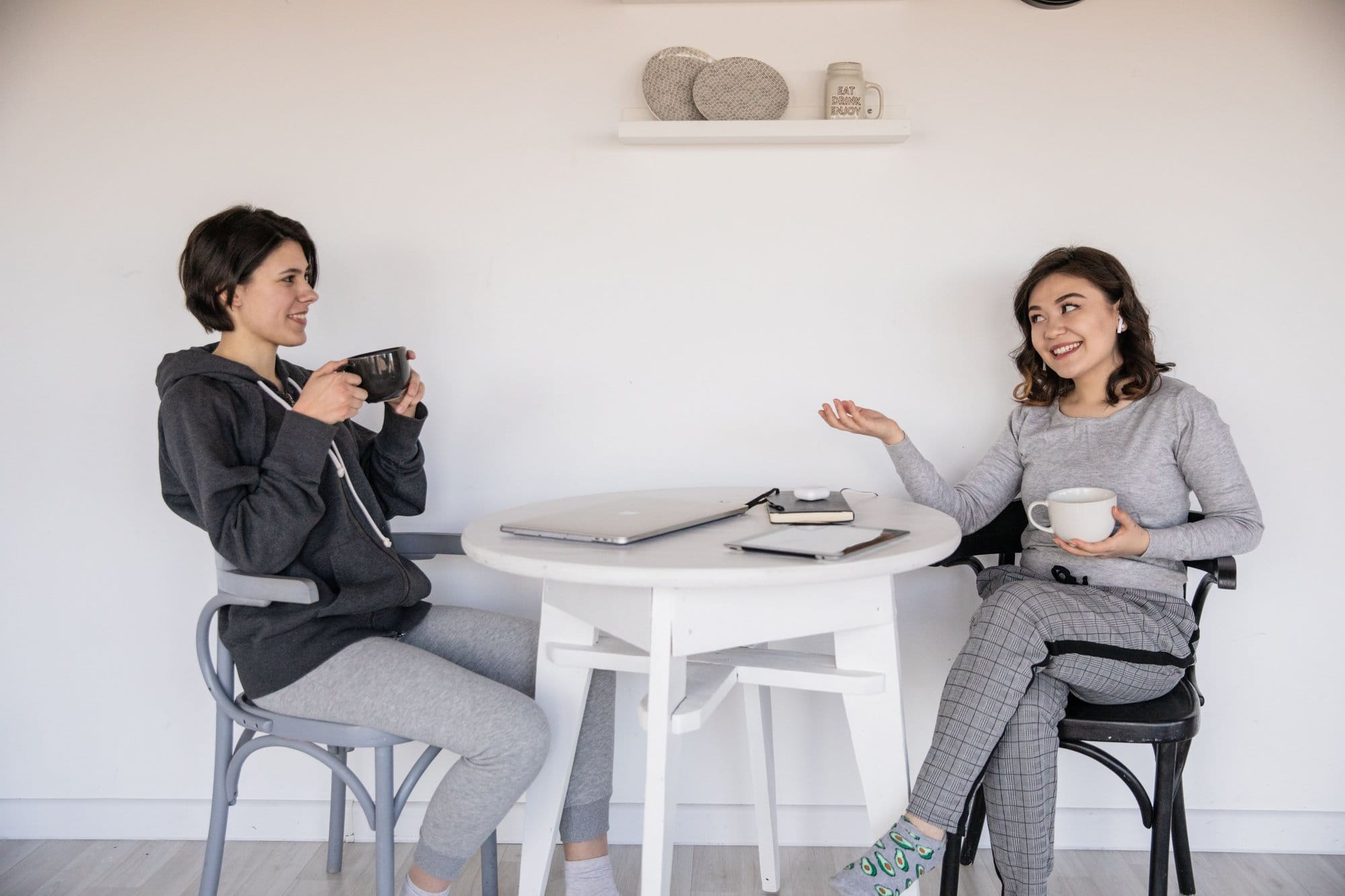 Două femei stau de vorbă la o masă, cu câte o cană de cafea